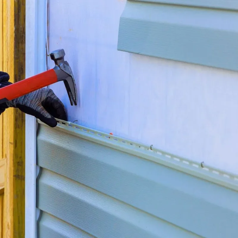 Siding replacement cost Calgary work as a contractor nails new vinyl siding over house wrap